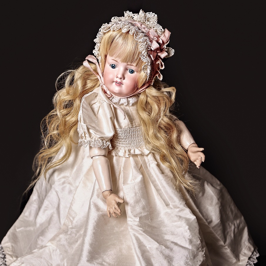 A vignette of a doll standing between two flowering plants in front of lacey sheers